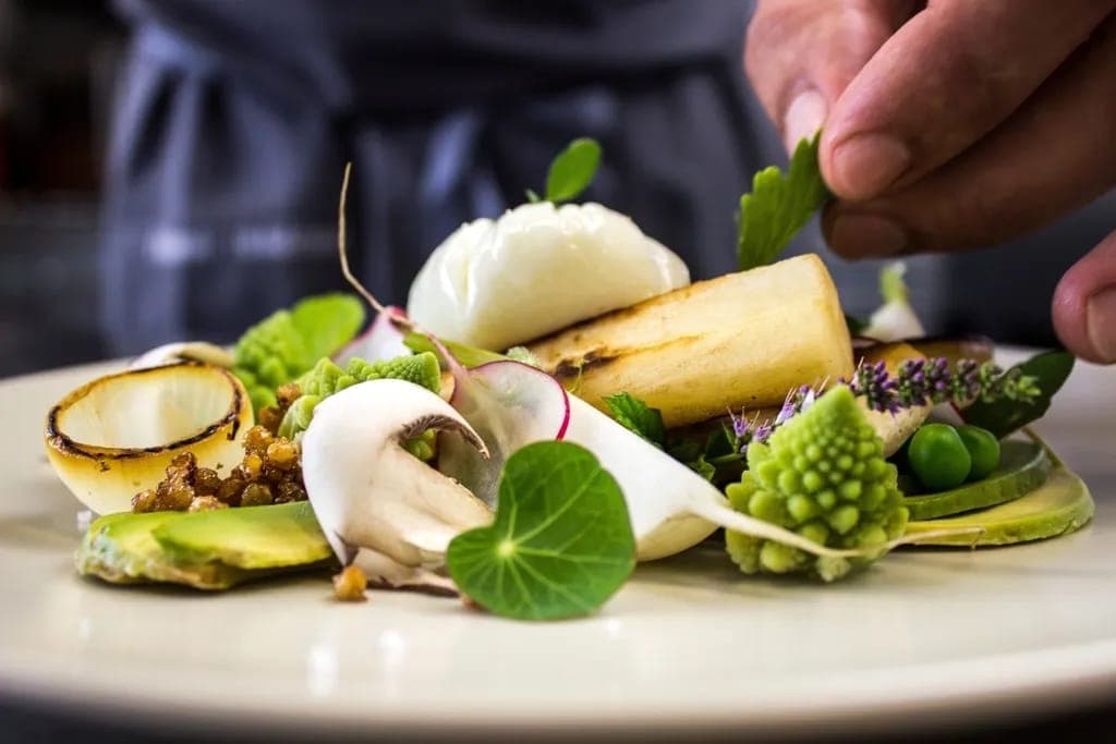 Les mains du chef posent une feuille de capucine sur une assiette de légumes et fleurs de menthe