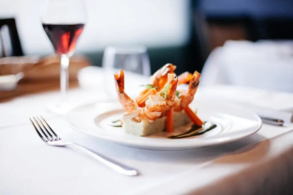 Gambas snackées sur purée, carottes glacées, verre de vin rouge