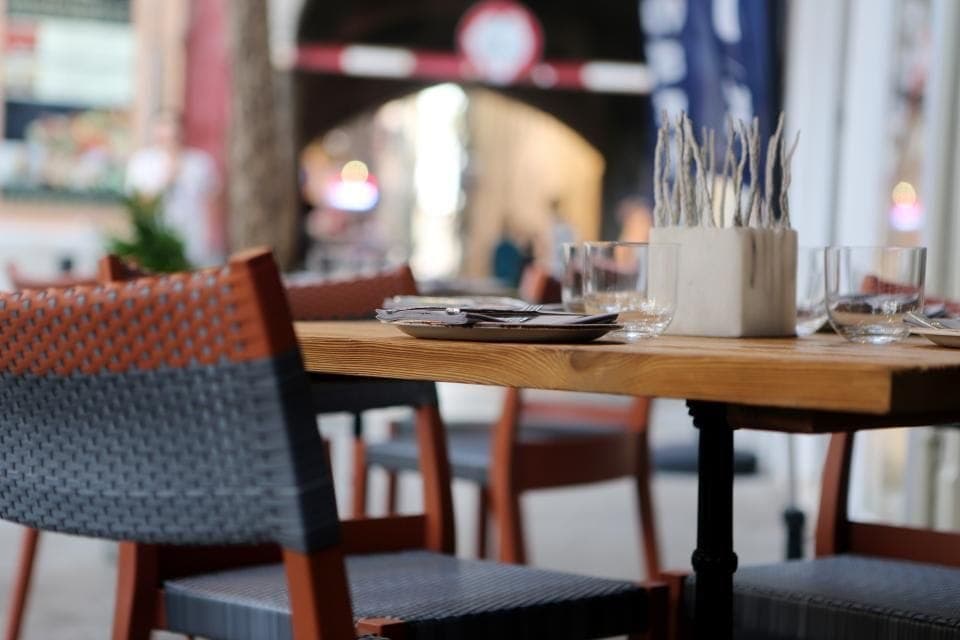 Table dressée en terrasse, verres et couverts posés sur le bois, chaises tressées